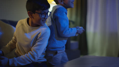 Two-Young-Boys-At-Home-Having-Fun-Playing-With-Computer-Games-Console-On-TV-Fighting-Over-Controllers-Late-At-Night-3